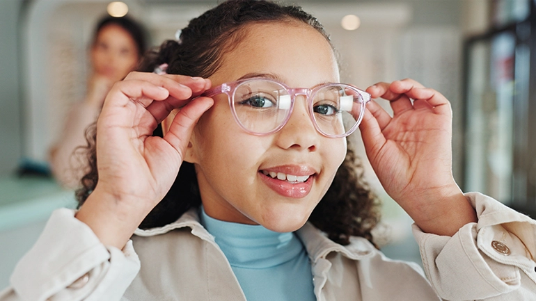 Grade school girl trying on new glasses at optometrist